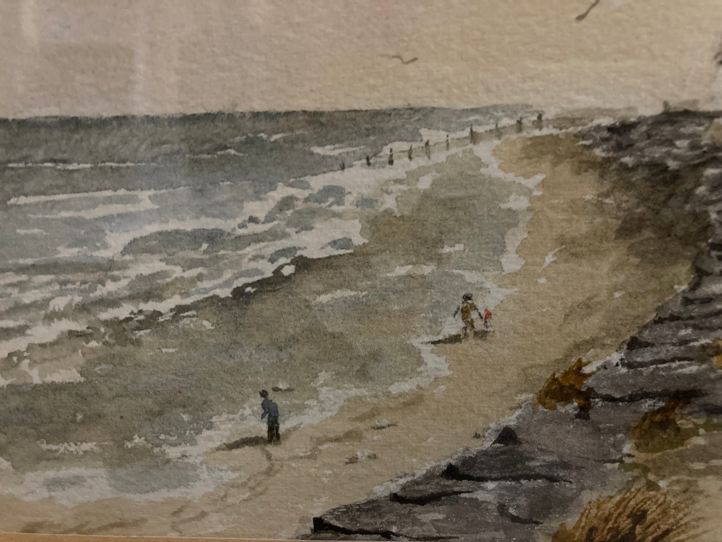 Two people walking along a sandy beach with the waves in the background.