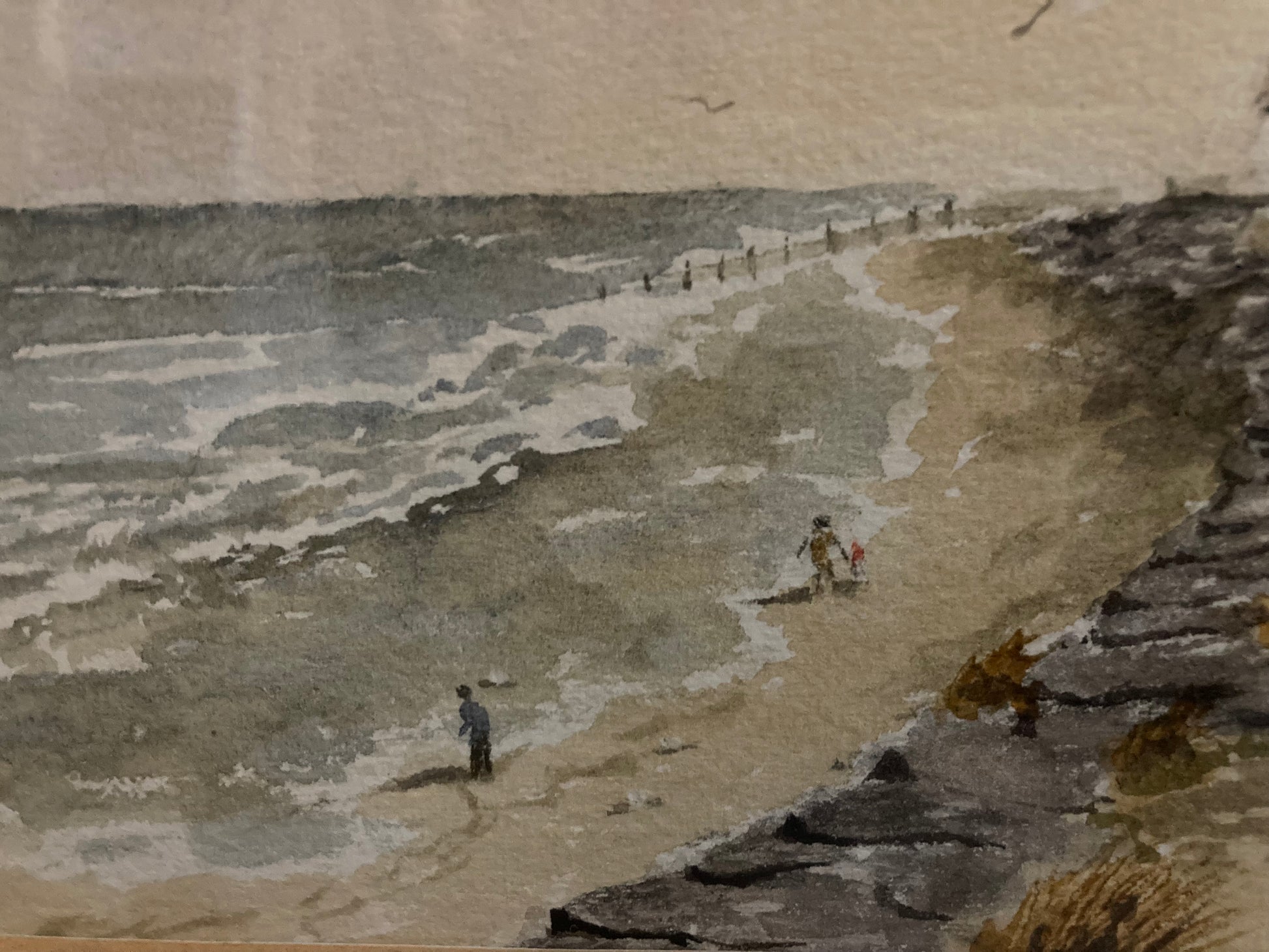 Two people walking along a sandy beach with the waves in the background.