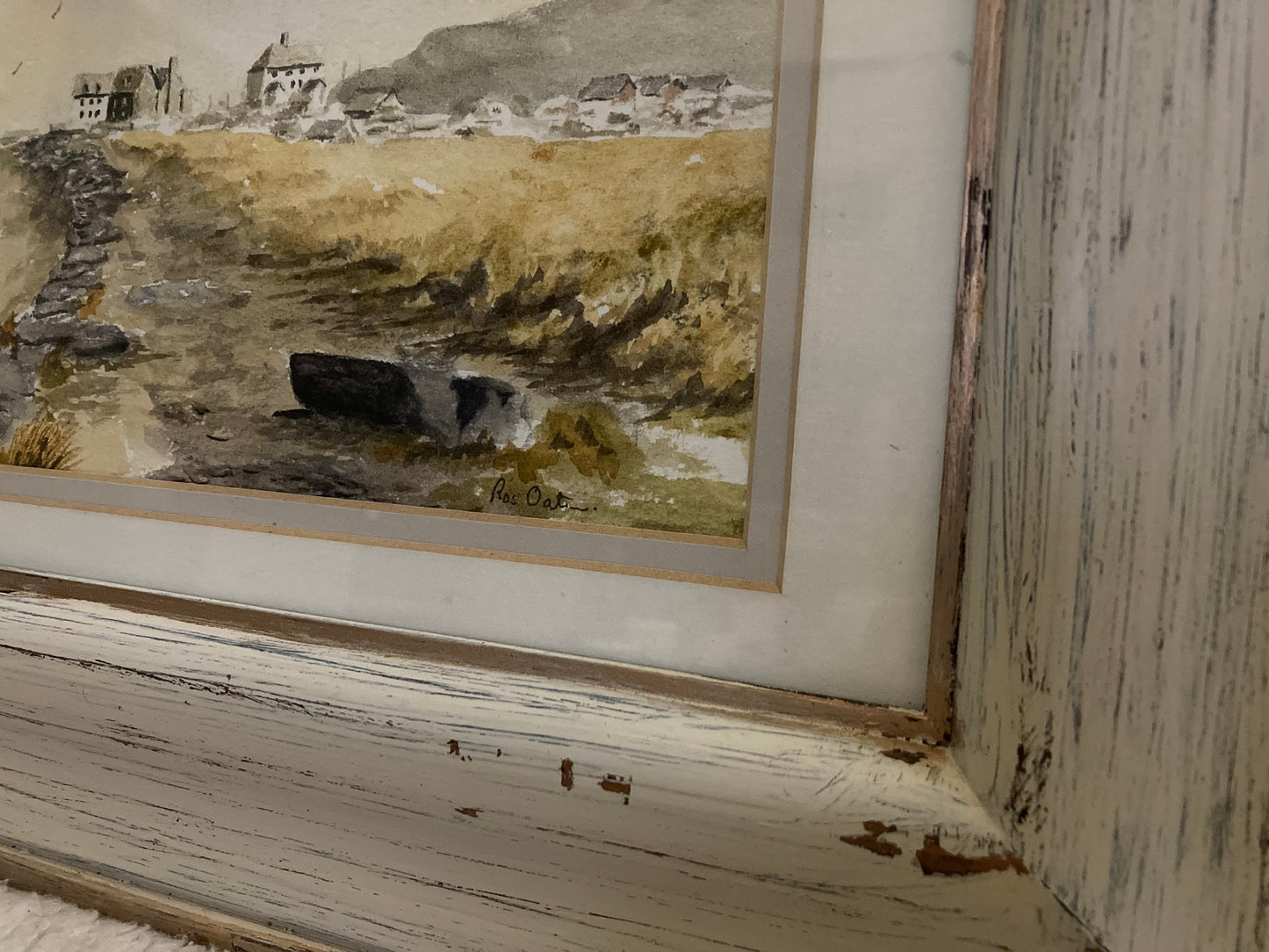 Framed watercolor painting of a coastal scene with rocky shoreline and buildings.