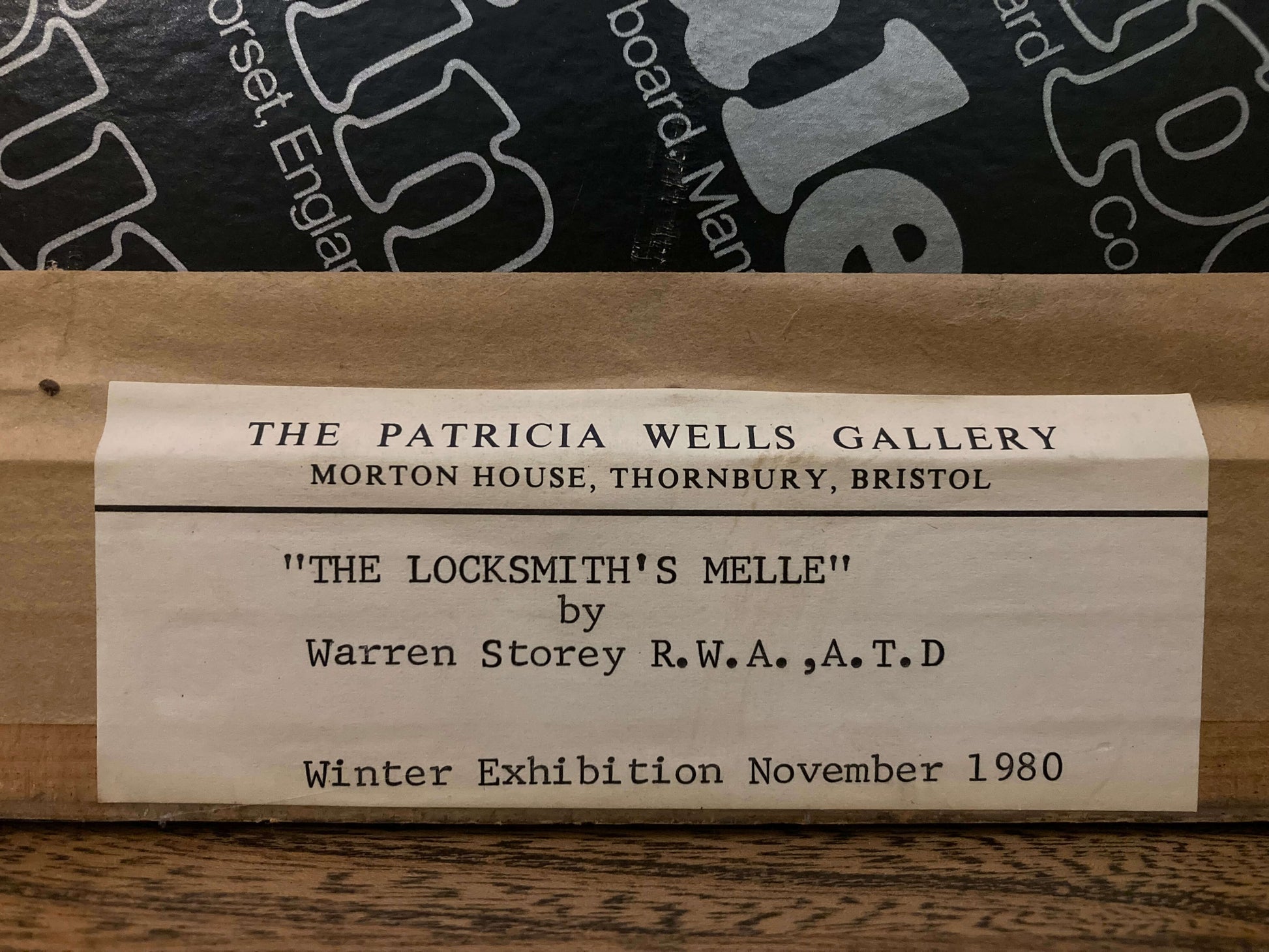 Wooden plaque with text about The Patricia Wells Gallery and an artwork by Warren Storey, displayed on a wooden surface.