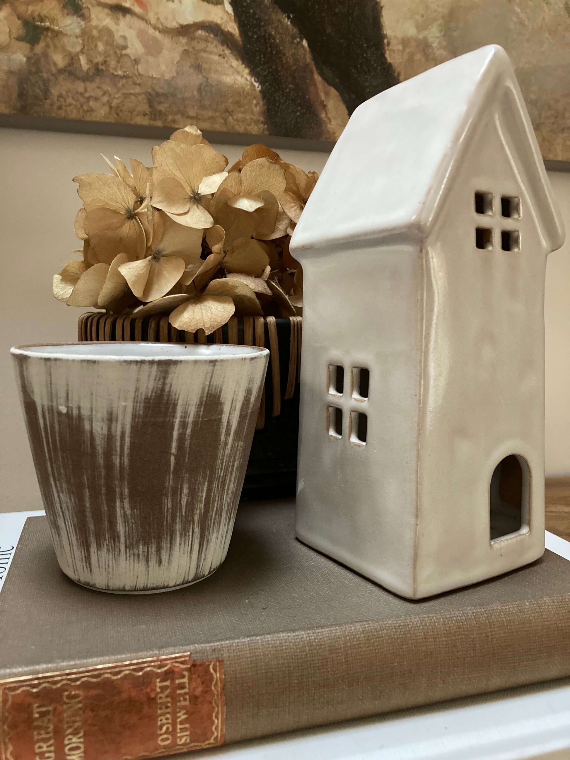 Ceramic house-shaped lantern and pot on a book with dried flowers