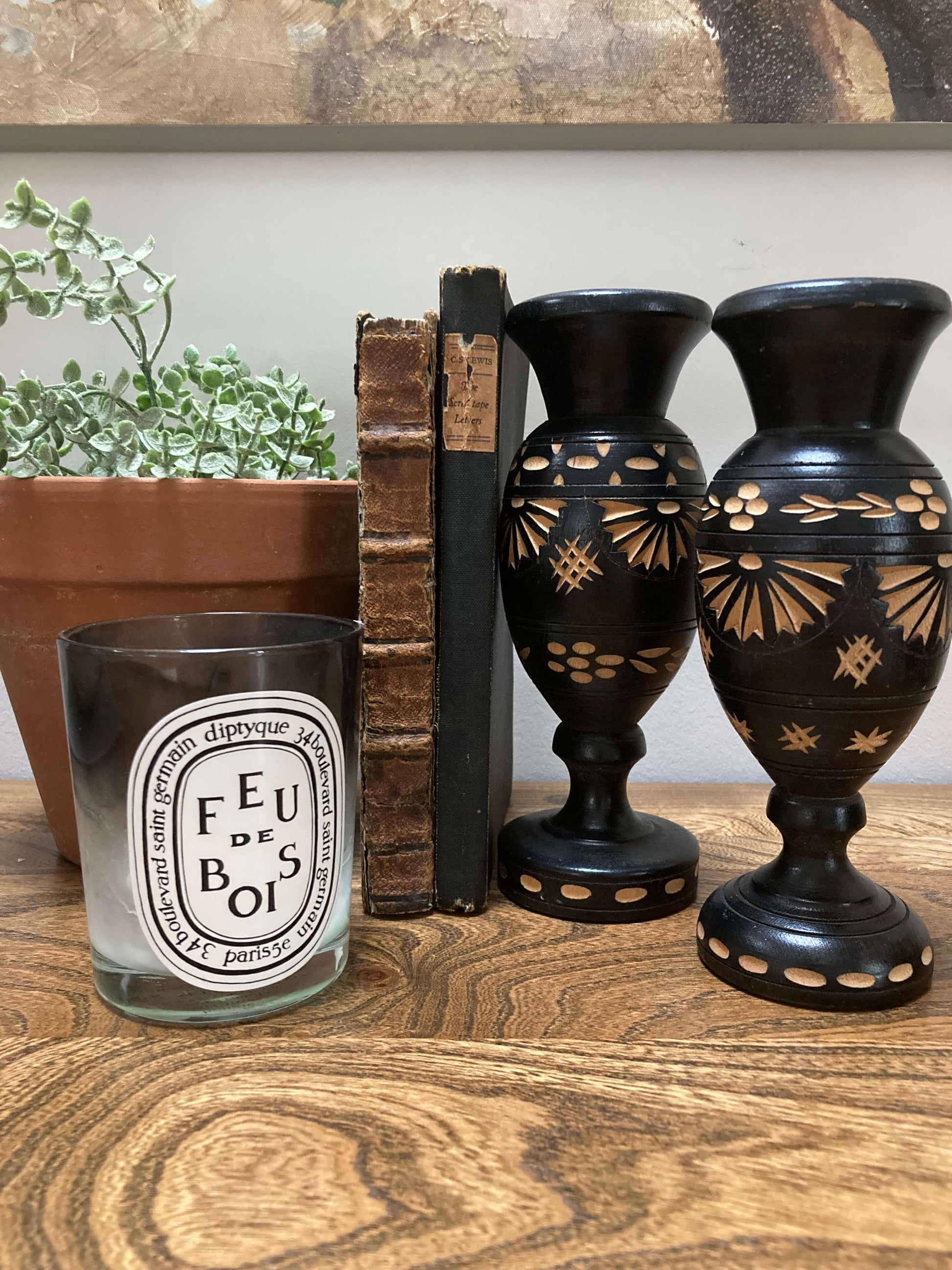 Decorative items including a candle, books, and black vases with gold patterns on a wooden surface.