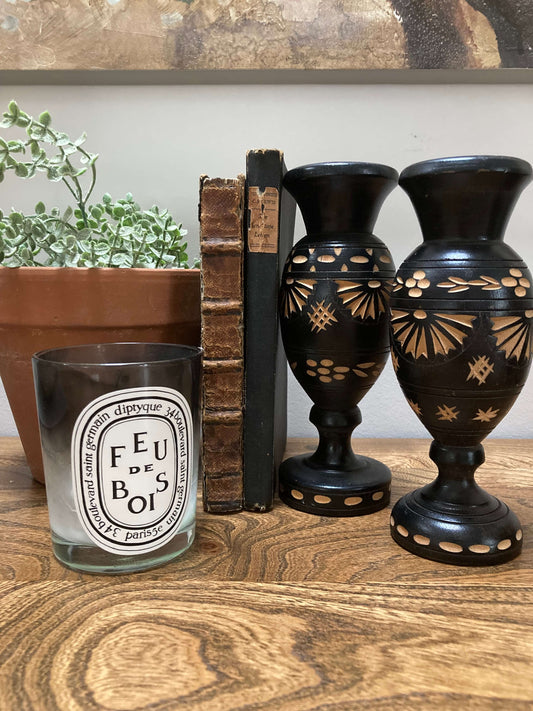 Decorative items including a candle, books, and black vases with gold patterns on a wooden surface.